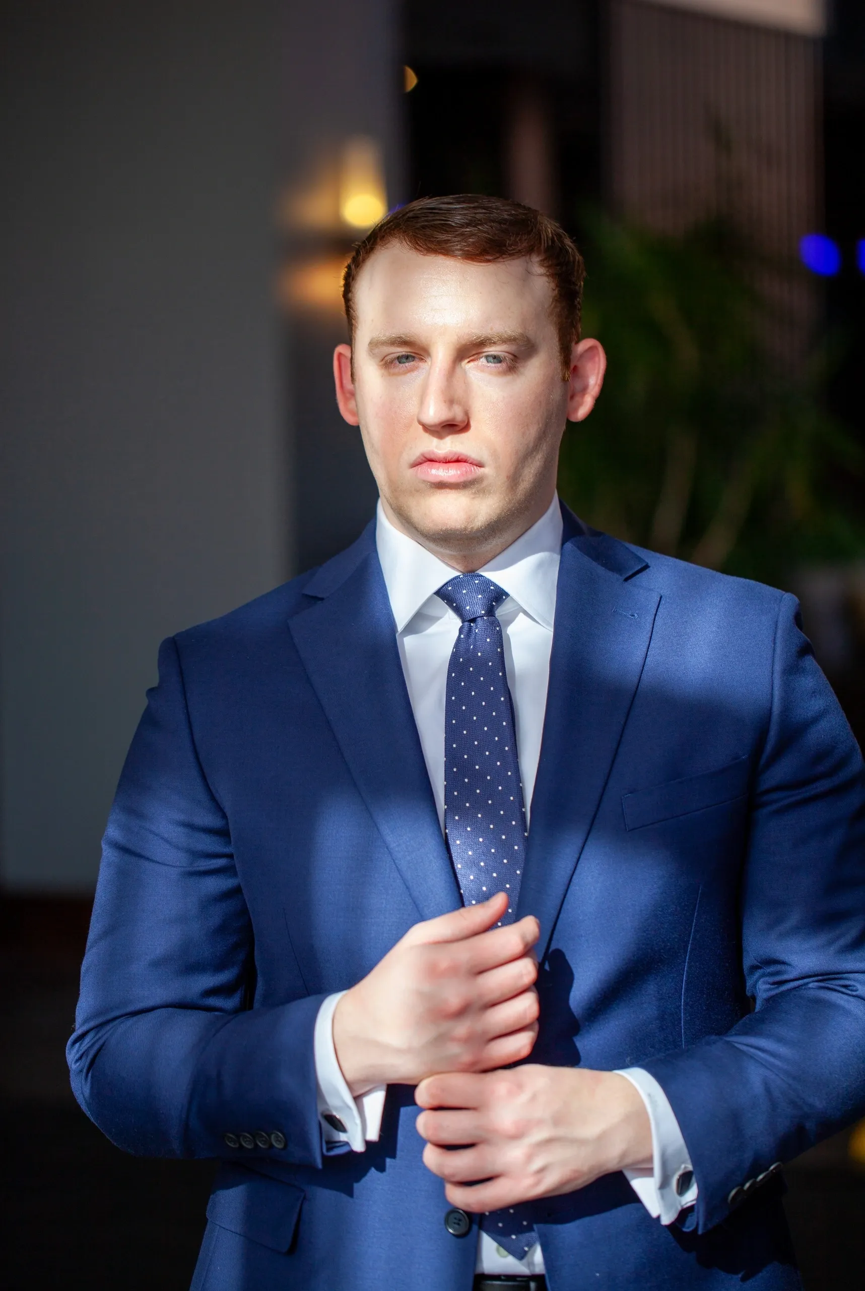 A man in a blue suit adjusting his jacket in a dimly lit setting.